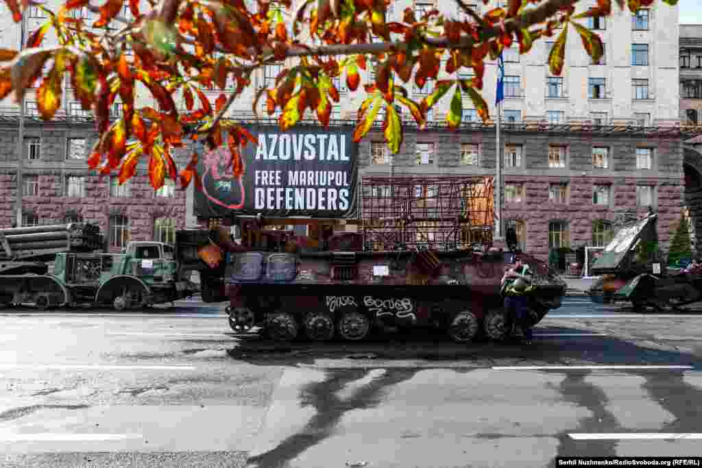 Сгоревший российский БТР на фоне плаката с призывом освободить из плена защитников Мариуполя и завода &quot;Азовсталь&quot;. Киев, 21 августа 2023 года &nbsp;