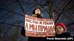 In November 2019, a woman in Moscow holds a  banner that demands Russia adopt a law against domestic violence. "They haven't killed us yet," the poster reads. 