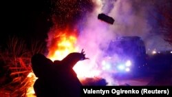 A demonstrator in Ukraine's Novi Sanzhary village throws a stone toward a police van during a February 20 protest against the arrival of evacuees from coronavirus-hit China. 