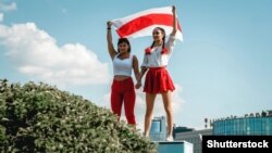 Two women display a former Belarusian national flag, a symbol of opposition to the government,  during a Minsk rally on August 16, 2020 against police violence and Belarus' official presidential election results.