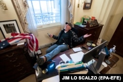 A supporter of President Donald Trump sits at the desk of U.S. House Speaker Nancy Pelosi (Democrat-California) after a pro-Trump mob stormed into the U.S. Capitol on January 6, 2021.