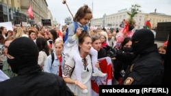 A woman carrying a girl confronts riot police  during a women's march in Minsk against election fraud and police violence on August 29, 2020. 