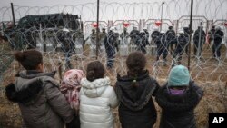 Migrant children stand in front of a barbed wire fence and Polish servicemen on the Belarusian side of Poland's Kuznitsa checkpoint  on November 17, 2021, as reports first surfaced of the migrants' withdrawal from the area, under Belarusian forces' supervision. 