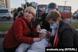 A law enforcement employee bandages the head of a woman injured in a crackdown by riot police on protesters in Minsk on September 23, 2020.