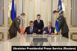 Ukrainian President Volodymyr Zelenskiy looks on while then Defense Minister Andriy Taran (right) and Baykar CEO Haluk Bayraktar sign a memorandum on September 29, 2021 to establish joint training and maintenance centers for Baykar's military drones.