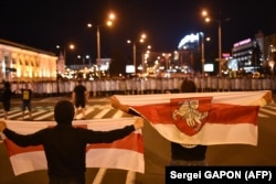 Demonstrators carrying flags with the coat of arms of Belarus' 1918 republic stand in front of riot police during a protest after polls closed in Belarus' presidential election, in Minsk on August 9, 2020. (Photo by Sergei GAPON / AFP)