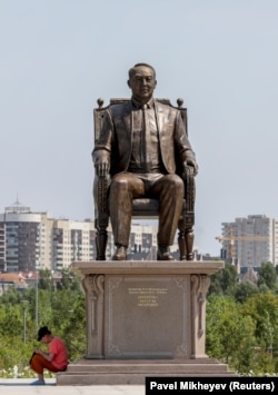 A woman sits at the base of a monument to Kazakh President Nursultan Nazarbaev in Nur-Sultan on July 4, 2021.